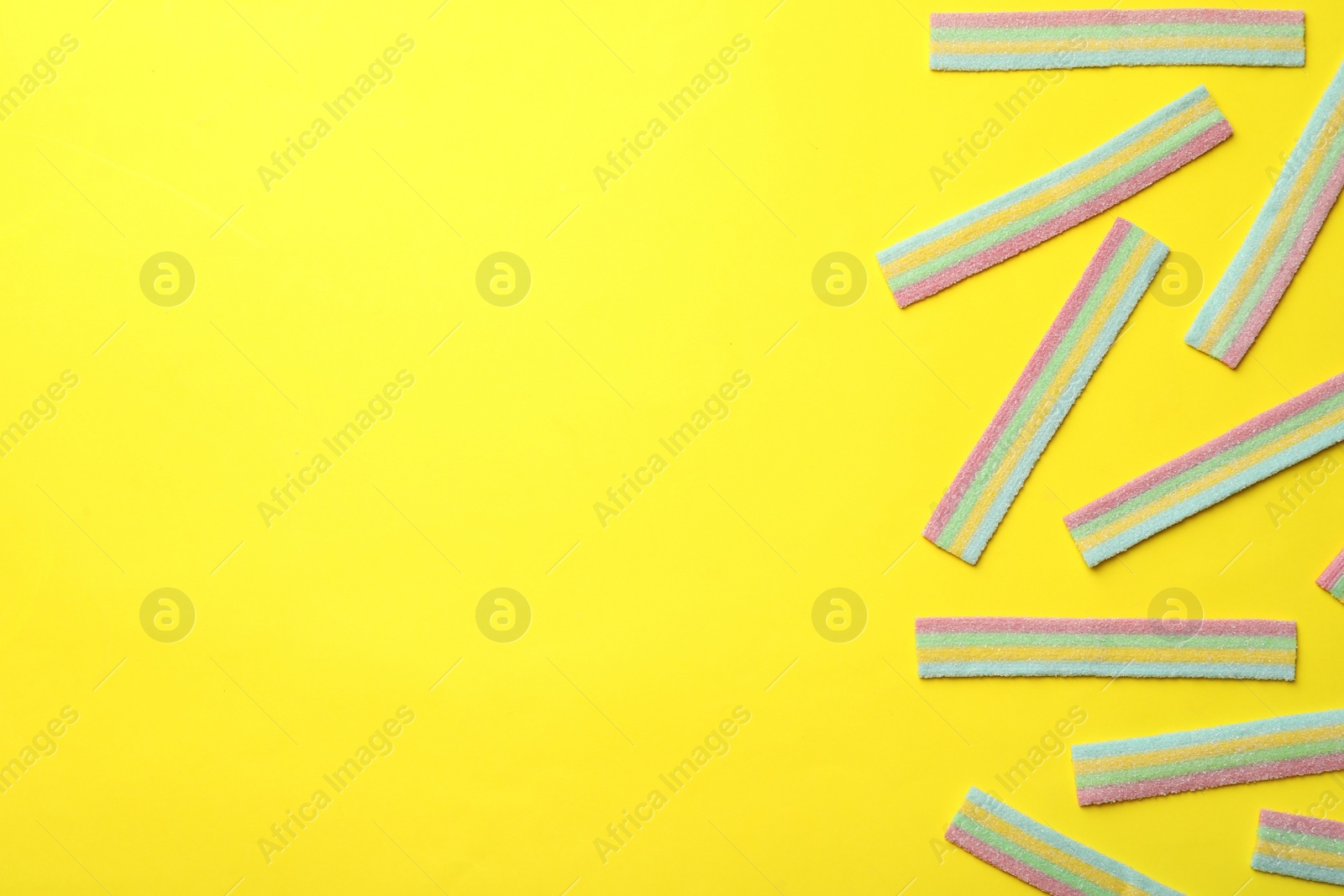 Photo of Delicious gummy candies on yellow background, flat lay. Space for text