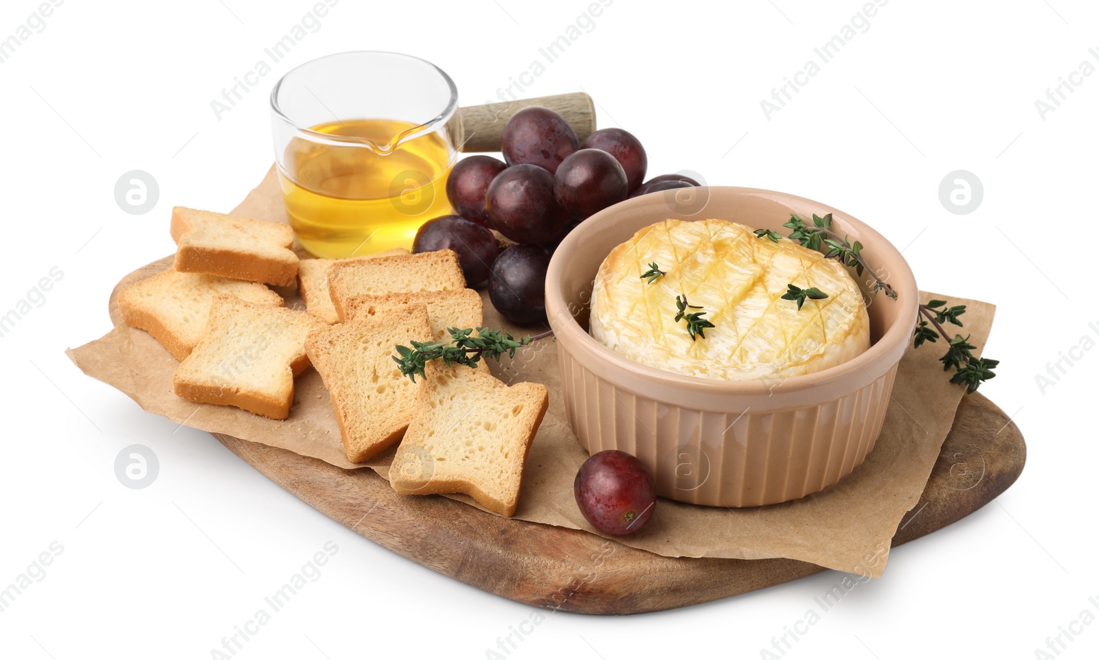 Photo of Tasty baked camembert in bowl, croutons, grapes, honey and thyme on white background