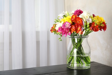 Photo of Vase with bouquet of spring freesia flowers on table in room. Space for text