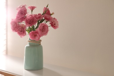 Photo of Bouquet of beautiful Eustoma flowers on table near light wall. Space for text