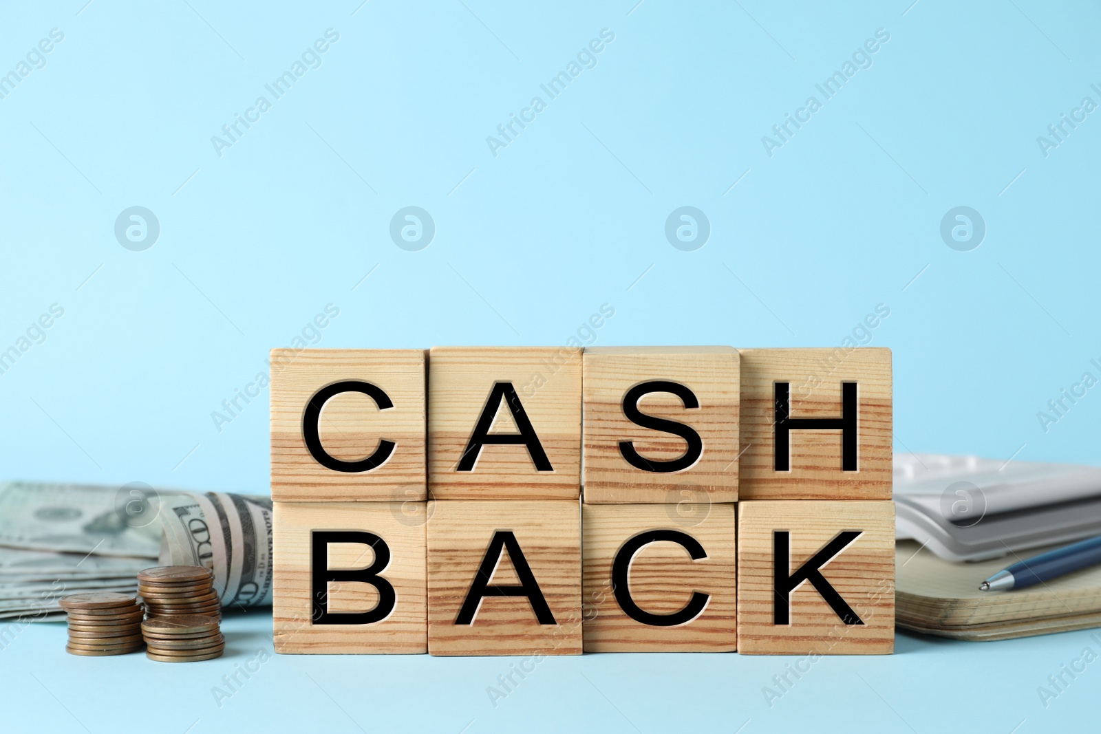 Photo of Word Cashback made with wooden cubes, coins and banknotes on light blue background