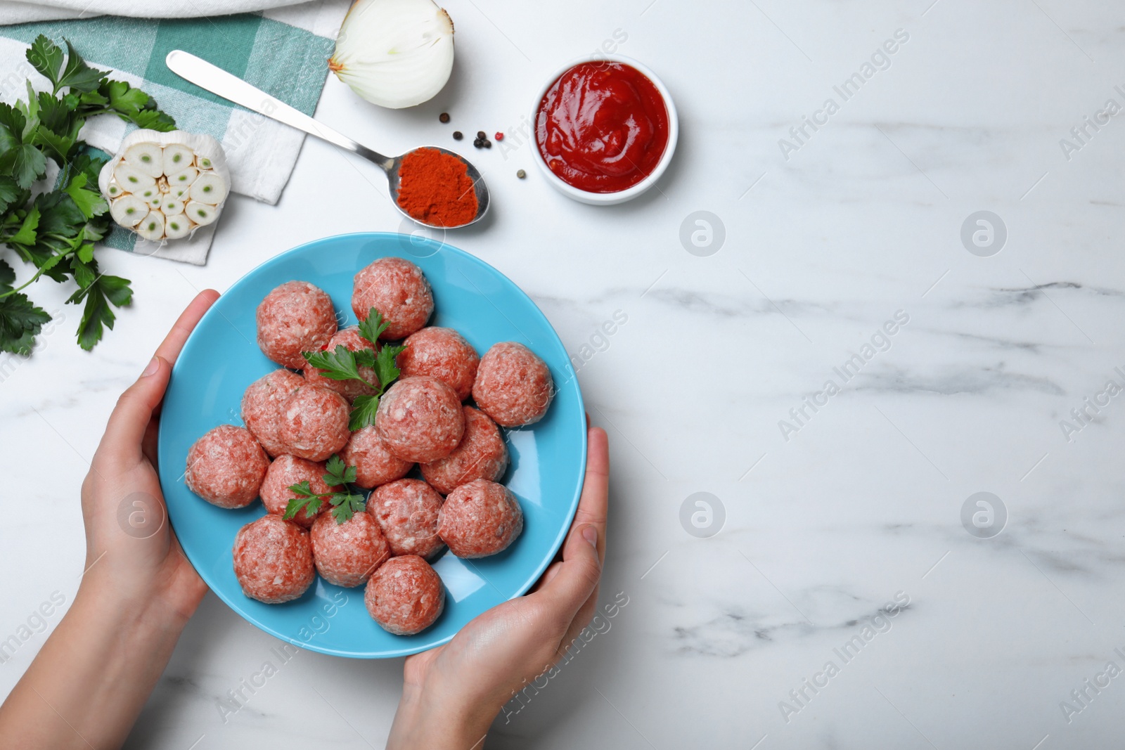 Photo of Woman holding plate with fresh raw meatballs at white table, top view. Space for text