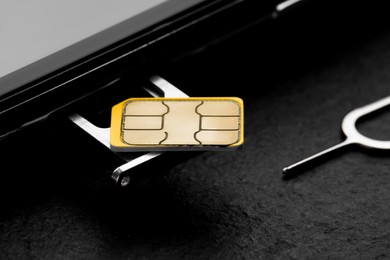 Photo of SIM card, mobile phone and ejector on black table, closeup