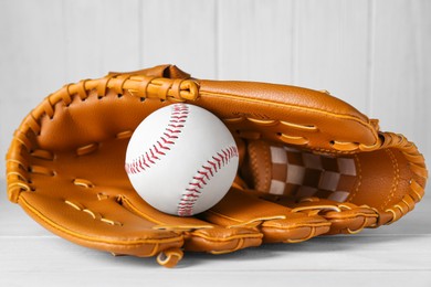 Photo of Leather baseball glove with ball on white wooden table