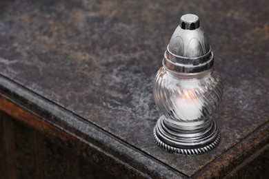 Photo of Grave lantern with burning candle on granite surface in cemetery, space for text