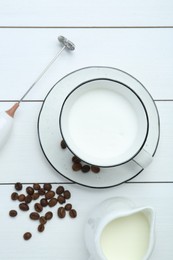 Photo of Flat lay composition with mini mixer (milk frother), whipped milk and coffee beans on white wooden table