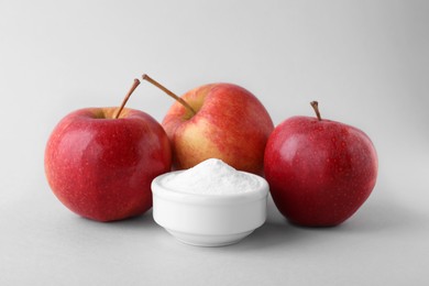 Photo of Bowl with sweet fructose powder and ripe apples on white background