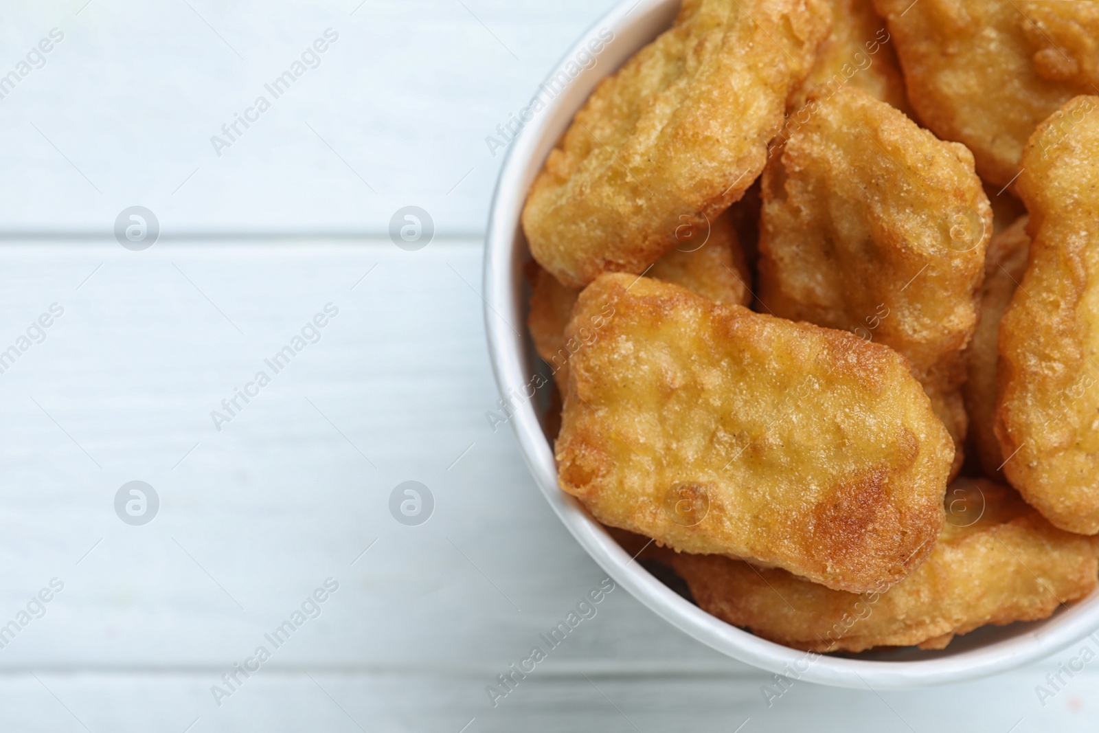 Photo of Bucket with tasty chicken nuggets on white wooden table, top view. Space for text