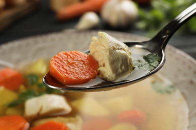 Spoon with fresh homemade chicken soup on blurred background, closeup