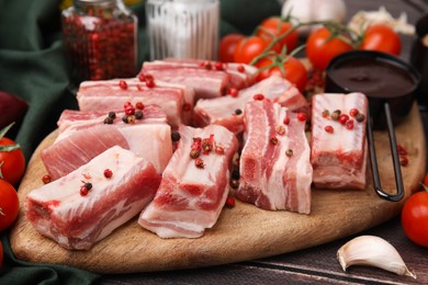Photo of Cut raw pork ribs with peppercorns on wooden table, closeup