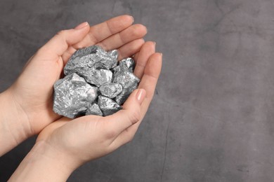 Photo of Woman with silver nuggets at grey table, closeup. Space for text