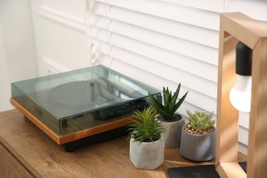 Stylish turntable with vinyl record on wooden chest of drawers indoors