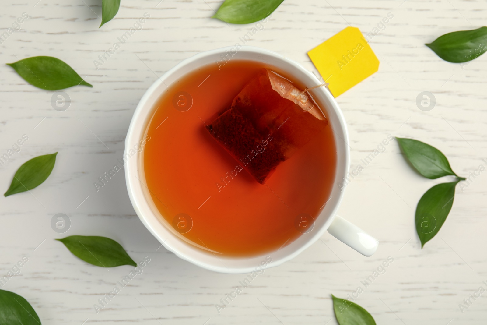 Photo of Cup of delicious tea with green leaves on wooden background, top view