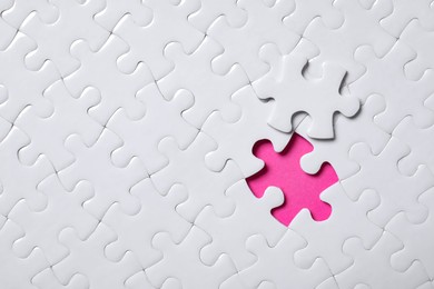 Photo of Blank white puzzle with separated piece on pink background, top view. Space for text