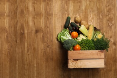 Different fresh ripe vegetables and crate on wooden table, top view. Space for text