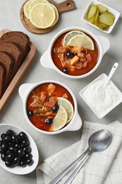 Photo of Meat solyanka soup with sausages, olives and vegetables served on white textured table, flat lay