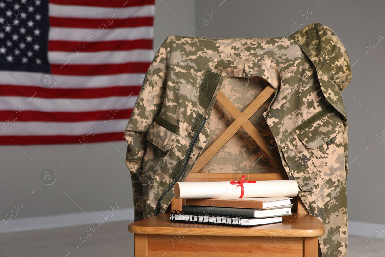 Photo of Chair with soldier uniform, notebooks and diploma near flag of United States indoors. Military education