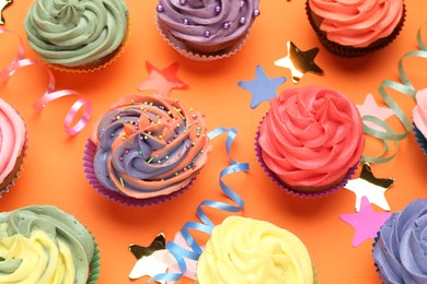 Delicious cupcakes with bright cream and party decor on orange background, flat lay