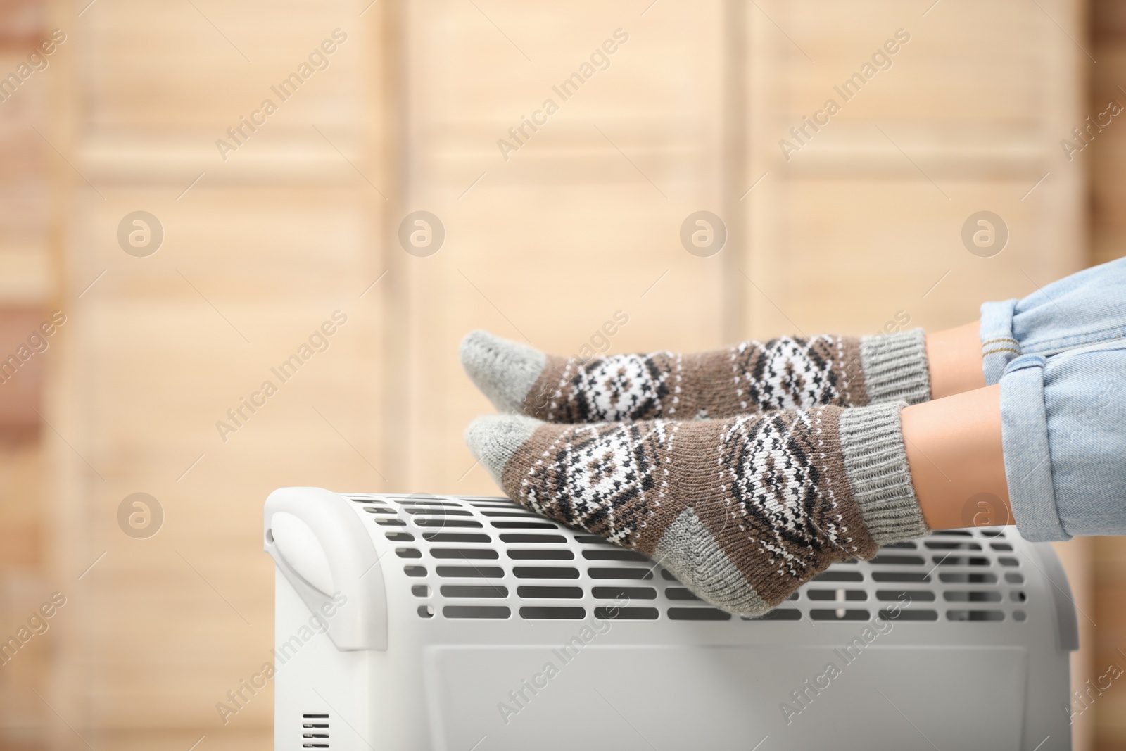 Photo of Woman warming feet on electric heater at home, closeup