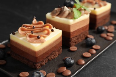 Pieces of triple chocolate mousse cake on black table, closeup