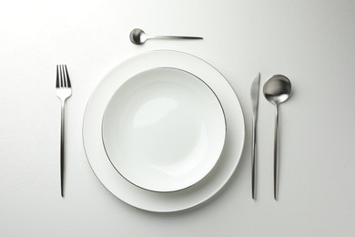 Photo of Stylish setting with cutlery and plate on white textured table, flat lay
