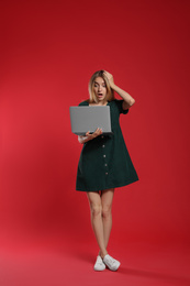 Full length portrait of emotional woman with modern laptop on red background