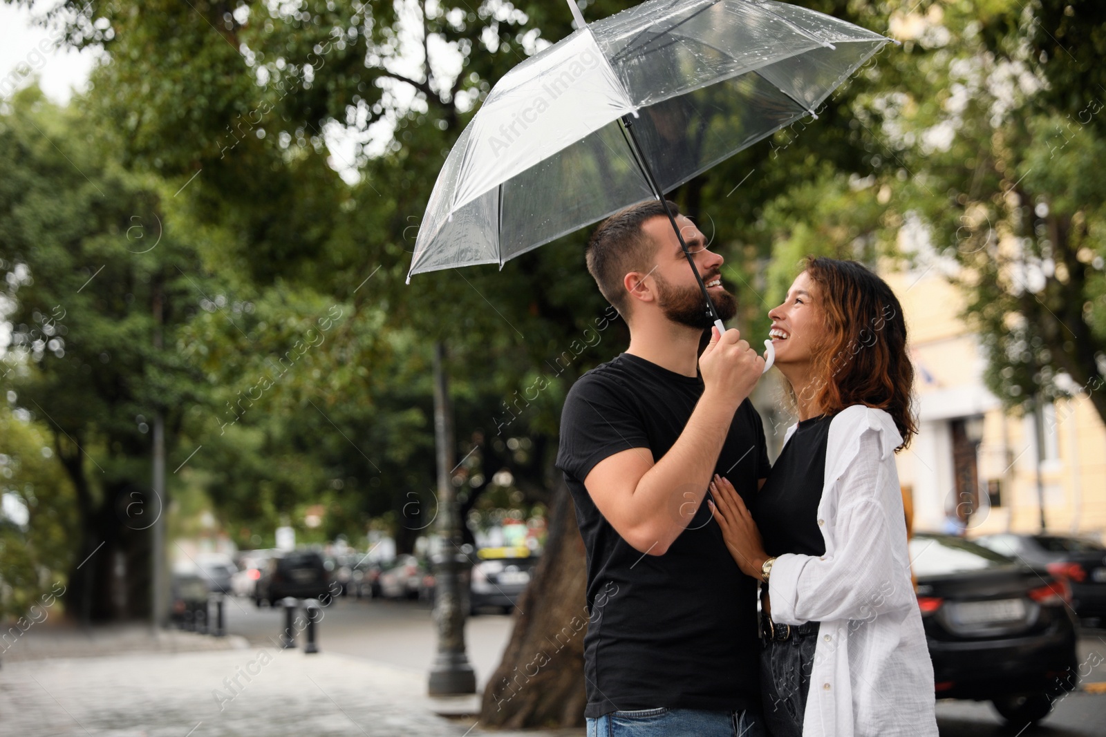 Photo of Young couple with umbrella enjoying time together under rain on city street, space for text