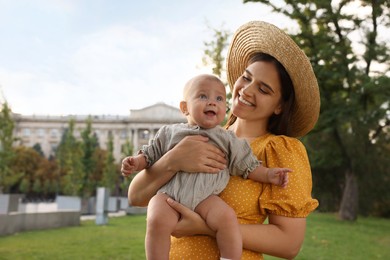 Happy mother with adorable baby walking in park on sunny day, space for text