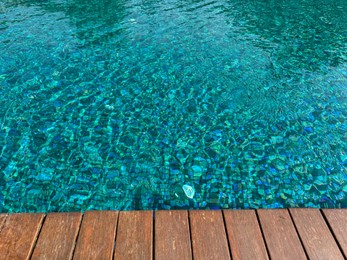 Photo of Clear rippled water in swimming pool and wooden deck outdoors. Space for text