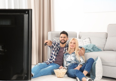 Photo of Young couple with bowl of popcorn watching TV on floor at home
