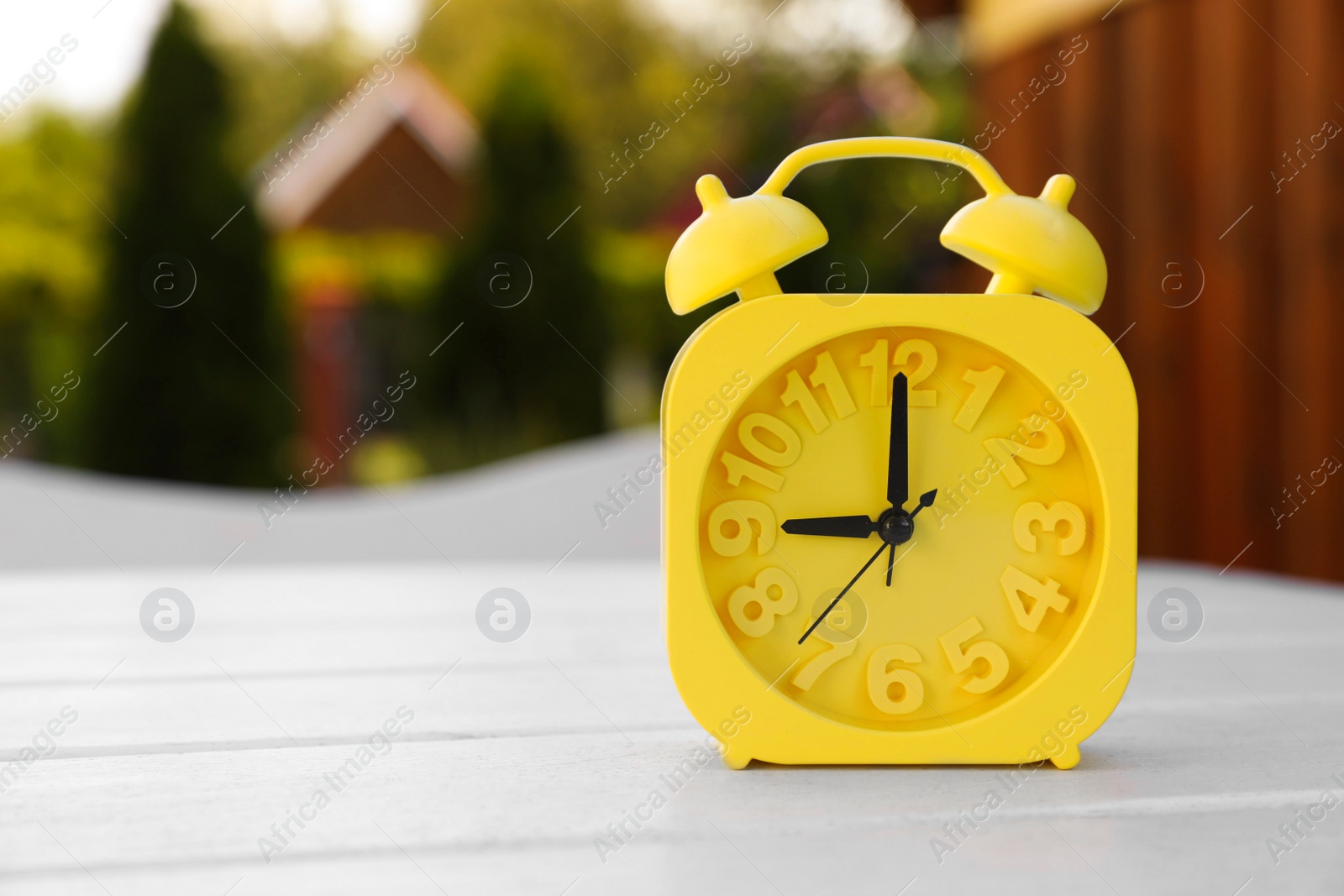 Photo of Yellow alarm clock on white wooden table outdoors at sunny morning. Space for text