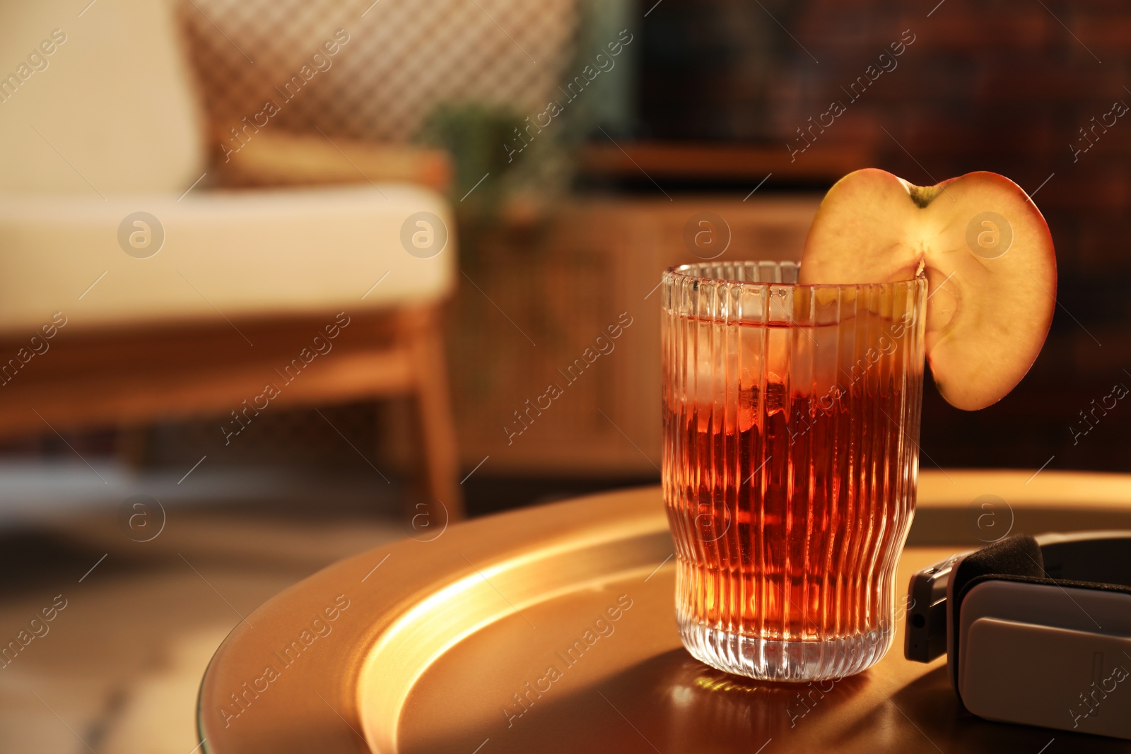 Photo of Glass of tasty cider and headphones on table in room, space for text. Relax at home