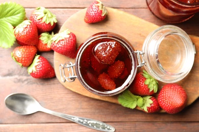 Delicious pickled strawberry jam and fresh berries on wooden table, flat lay