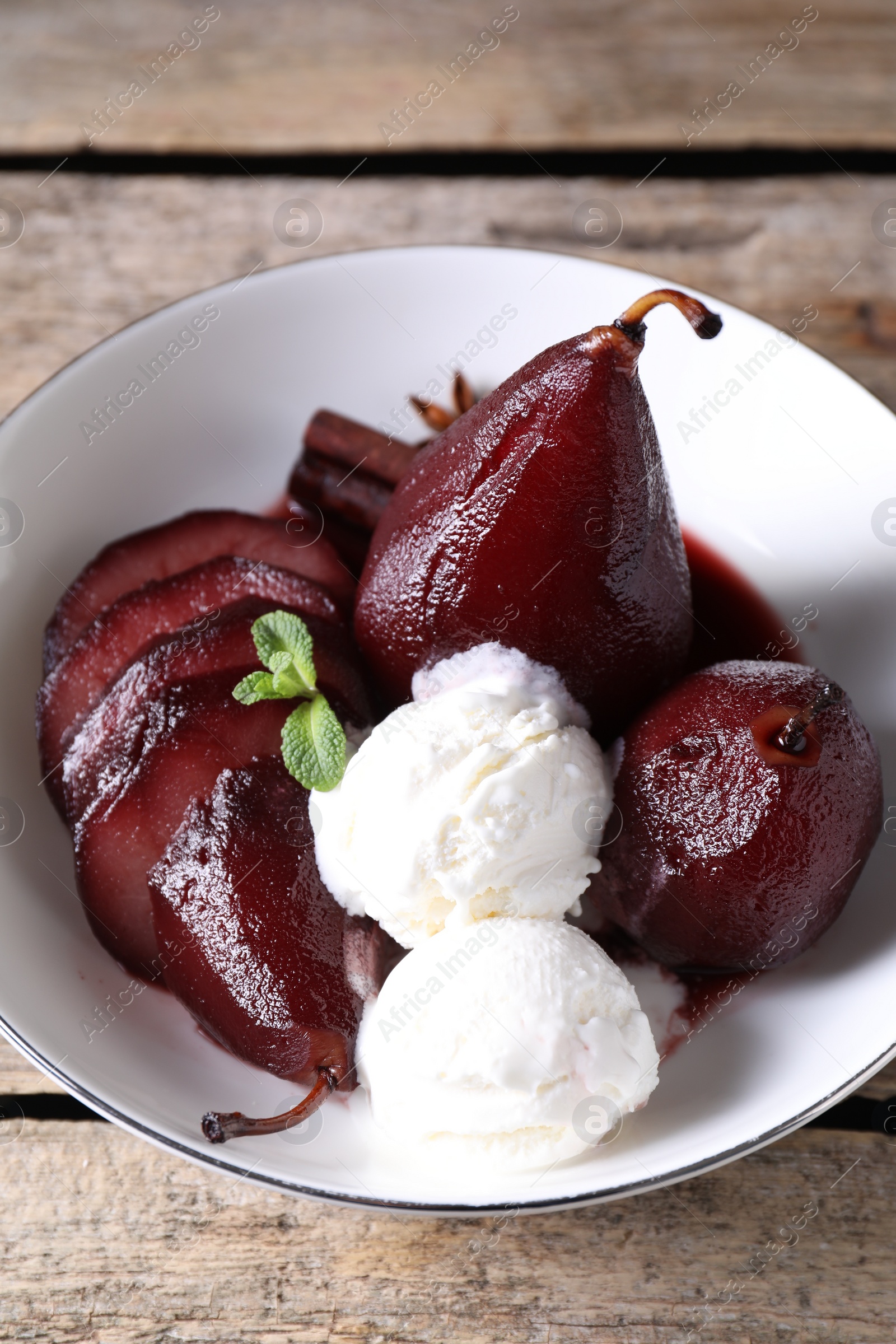 Photo of Tasty red wine poached pears and ice cream in bowl on wooden table, above view