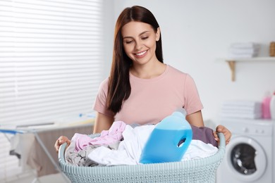 Woman holding basket with dirty clothes and fabric softener in bathroom