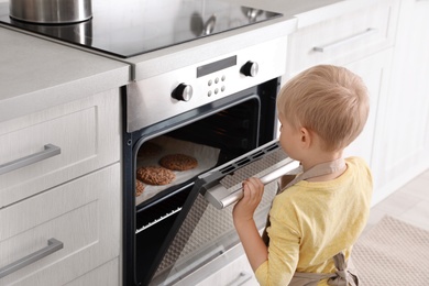Photo of Little boy baking cookies in oven at home