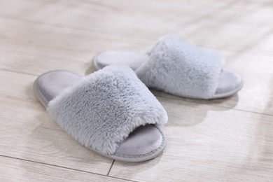 Photo of Grey soft slippers on light wooden floor at home, closeup