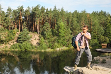 Photo of Young man on rock near lake and forest. Camping season