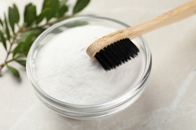 Photo of Bamboo toothbrush and glass bowl of baking soda on light table, closeup