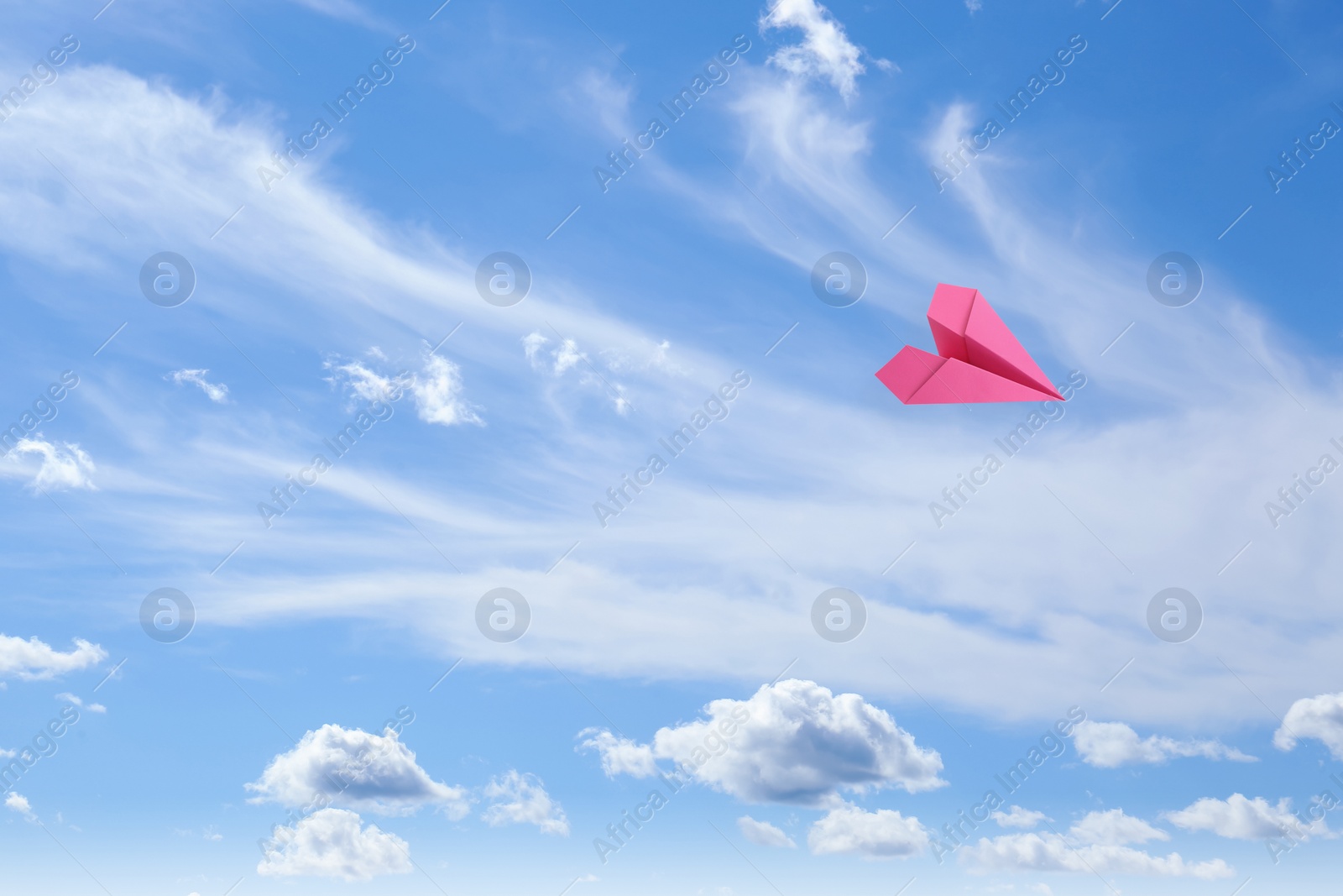 Image of Pink paper plane flying in blue sky with clouds