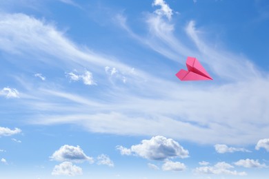 Image of Pink paper plane flying in blue sky with clouds