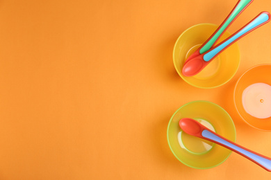 Photo of Set of colorful plastic dishware on orange background, flat lay with space for text. Serving baby food