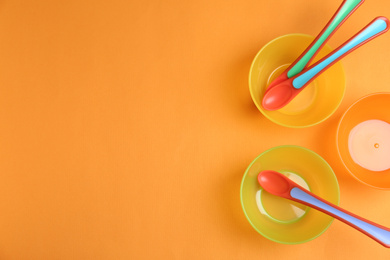 Set of colorful plastic dishware on orange background, flat lay with space for text. Serving baby food