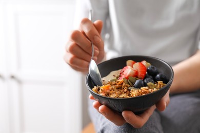 Photo of Woman eating tasty granola with berries, yogurt and seeds indoors, closeup. Space for text