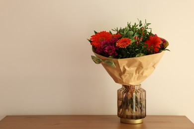 Photo of Bouquet of flowers on wooden table near white wall. Space for text