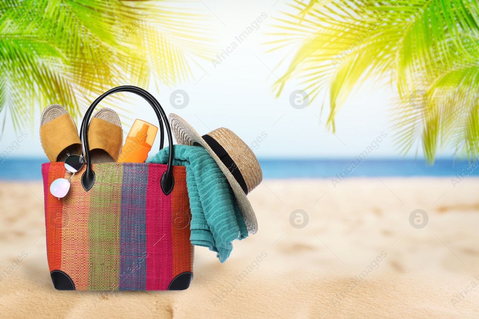 Image of Stylish bag with different accessories on tropical sandy beach, space for text 