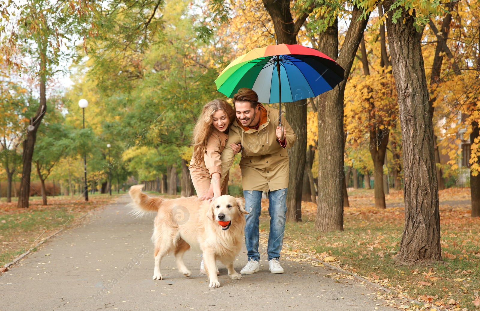 Photo of Young couple with umbrella and dog walking in park