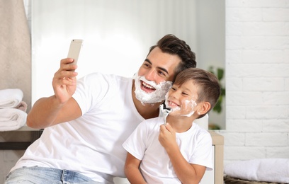 Father and son taking selfie while shaving in bathroom