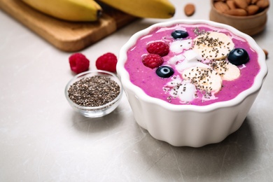 Delicious acai smoothie with fruits and coconut chips in dessert bowl on grey table