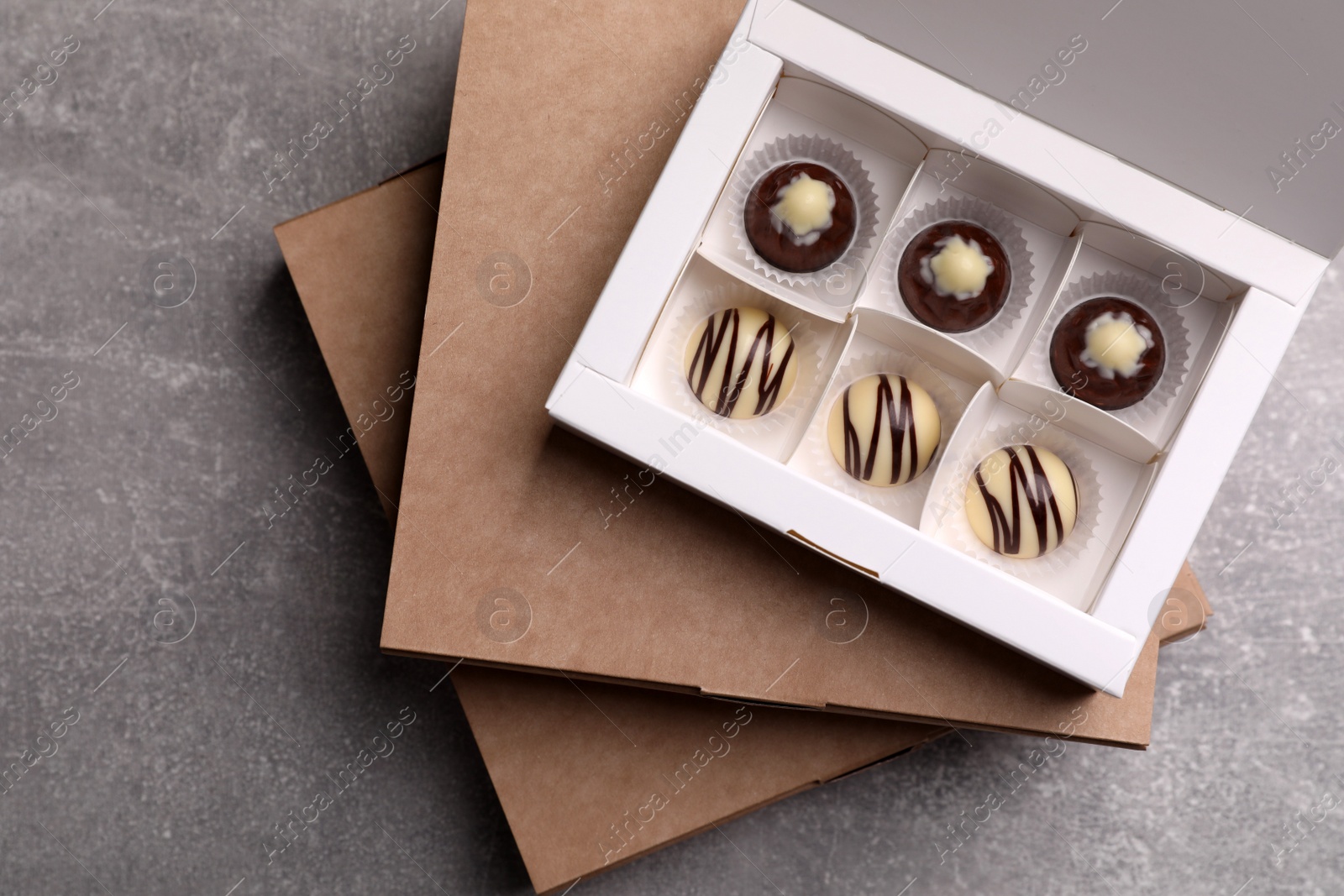 Photo of Delicious chocolate candies in box on light grey table, top view. Production line